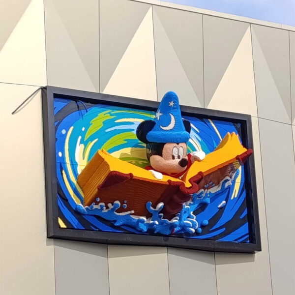 Mickey Mouse en brick d'art, portant une toque de sorcier, naviguant sur une mer de couleurs vives, créée avec des briques LEGO ou similaires, pour une décoration ludique et artistique.