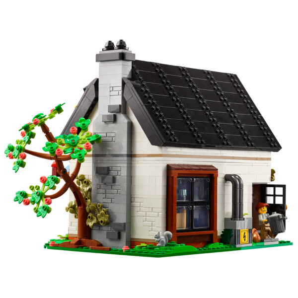 Maison en briques LEGO avec cheminée, fenêtre, arbre en fleurs, personnage lego avec valise, et éléments d'isolation solaire sur le toit. Parfait pour la décoration intérieure ou extérieure, idéale pour les amateurs de construction LEGO.